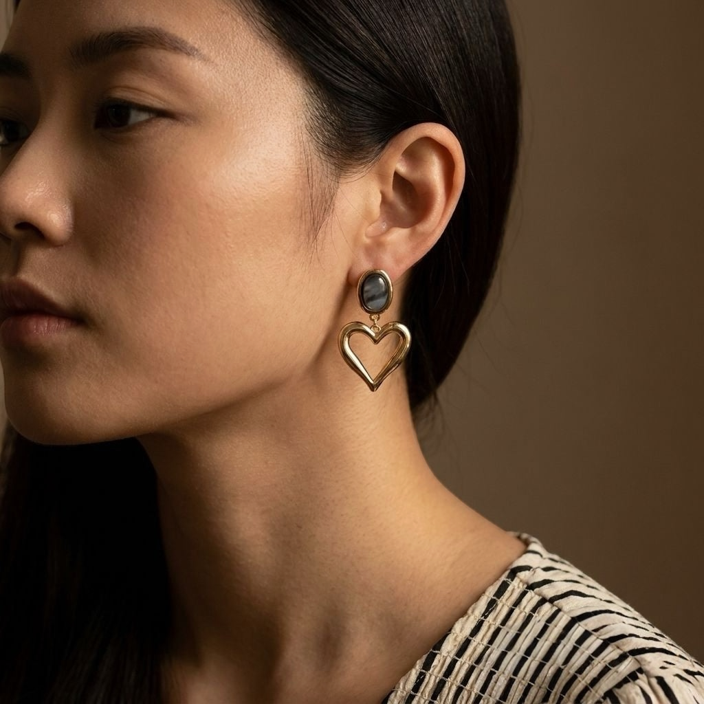 Loulu Jewellery gold-tone heart drop earrings with a black oval stone stud worn by a woman.