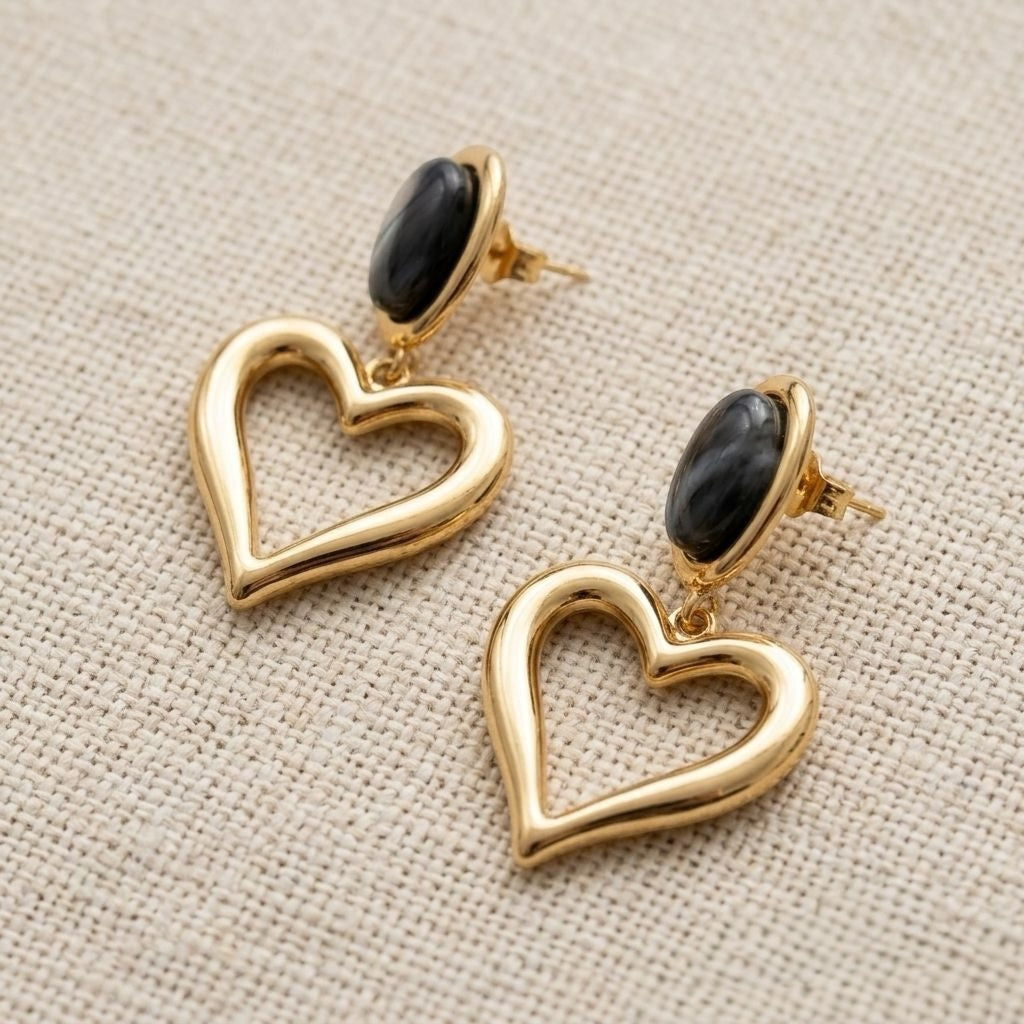 Loulu Jewellery gold-tone open heart drop earrings with black oval stone studs on a textured cream fabric background.