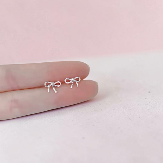 Loulu Jewellery delicate sterling silver bow stud earrings with a twisted rope-effect texture held on a fingertip