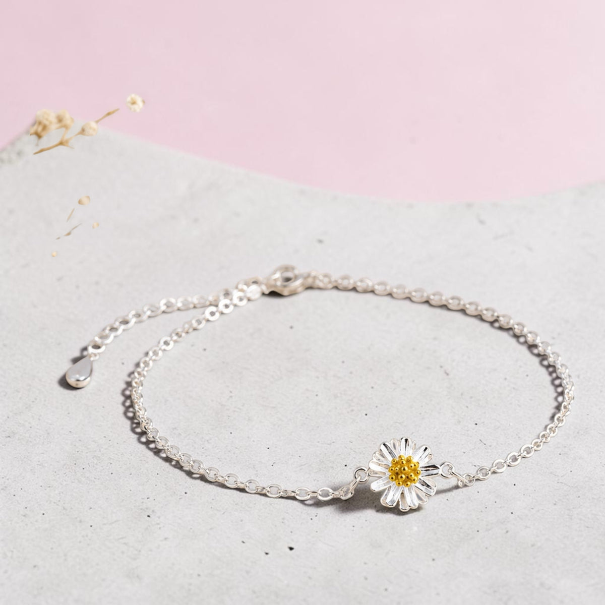 Loulu Jewellery silver-tone daisy charm anklet with white petals and a yellow centre on a grey textured surface